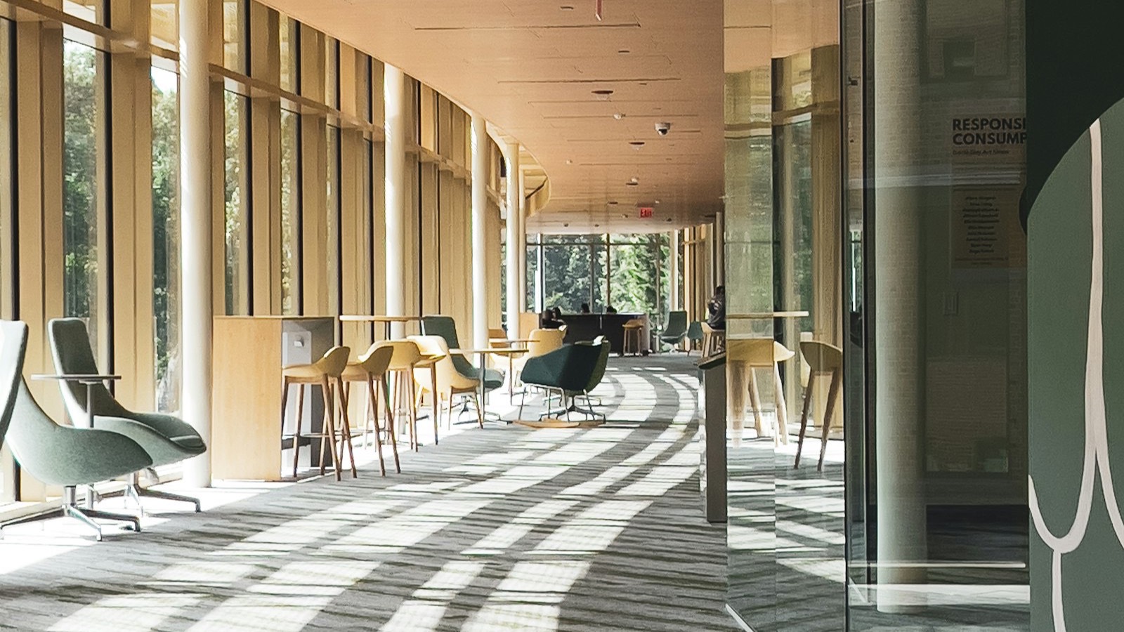 A long campus hallway with tables and chairs in window light.